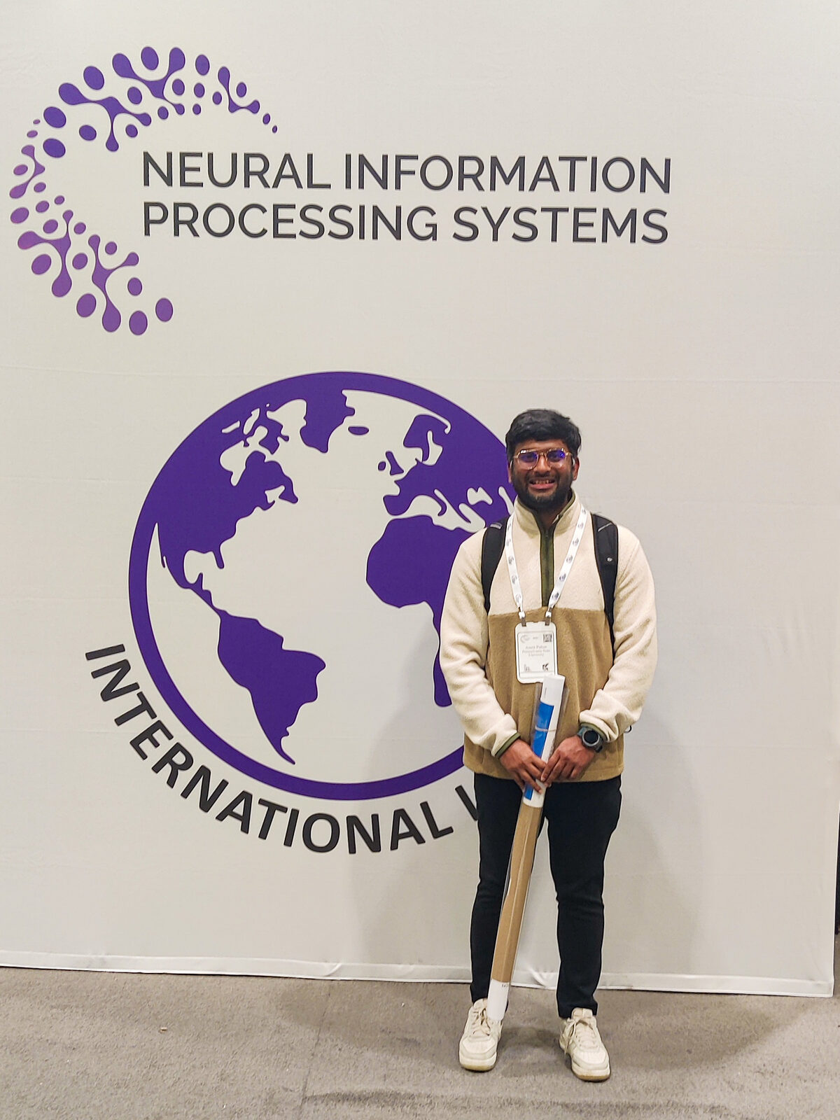 Me holding a poster tube in front of the NeurIPS banner